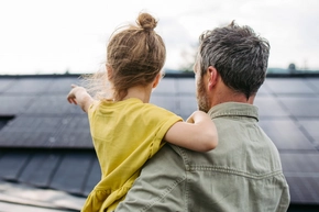 Mann mit Kind auf dem Arm, welches auf Photovoltaik zeigt